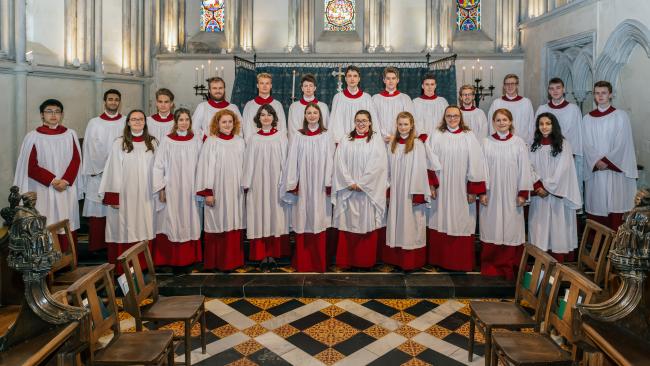 Choir members, wearing robes and standing in the College Chapel